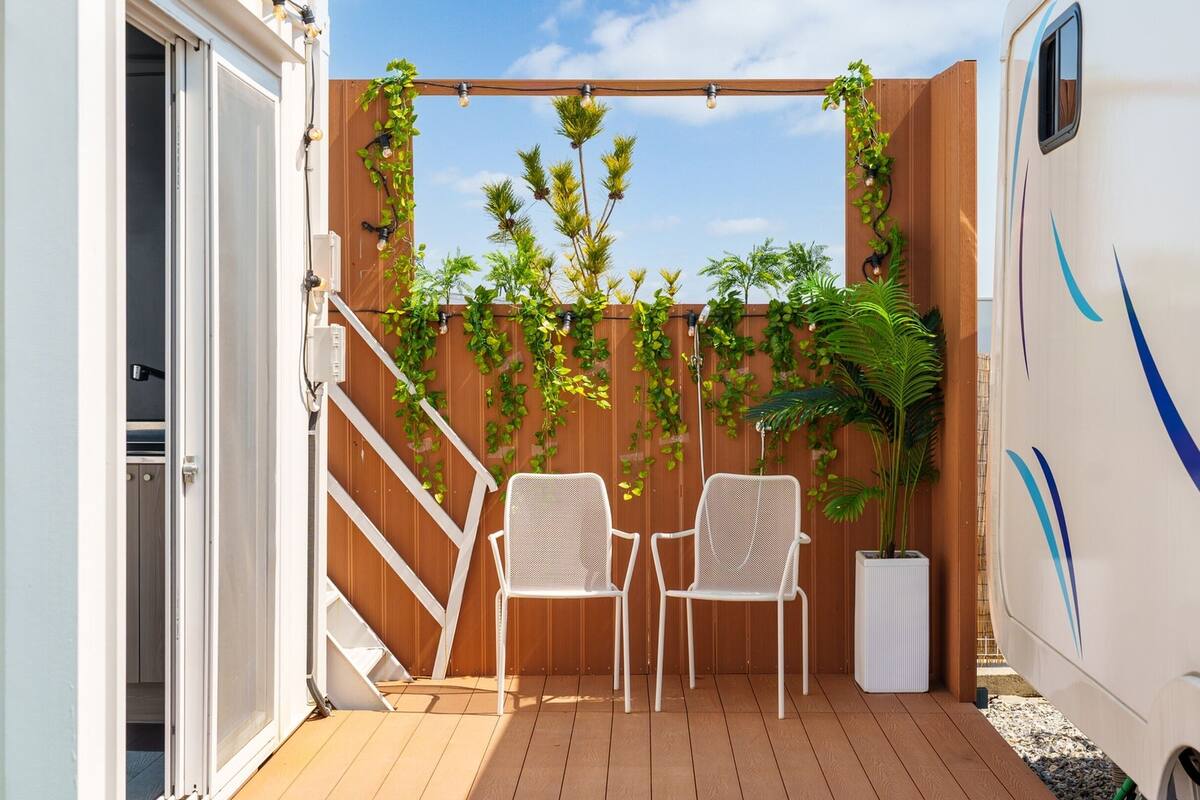 Un patio couvert avec deux chaises blanches, une clôture en bois et une plante en pot.