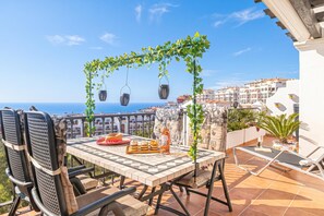 A terrace with a table set for dining, chairs, a hanging light fixture, and a view of the sea and buildings. - Calahonda Palmeras Best Views (Mijas)