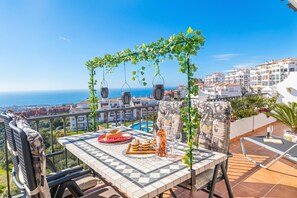Una terraza con mesa lista para comer, una piscina y vistas al mar y edificios.
