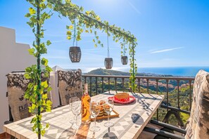 A table with a bottle, glasses, and pastries, overlooking a scenic landscape.