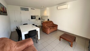 A compact living space with a kitchenette, a dining area with a white table and black chairs, a brown sofa, and a wooden bench.