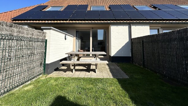 A house with a tiled roof, solar panels, a fenced backyard, and a patio area.