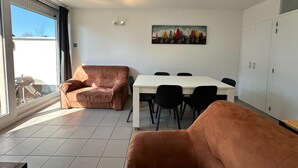 A modern living room with a large window, a dining table with chairs, and a sofa.