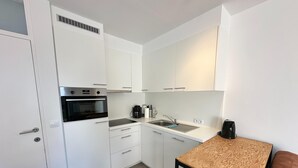 A compact kitchen with white cabinets, a built-in oven, a sink, and a coffee maker.