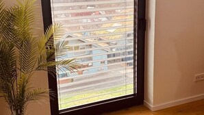 A room with a large sliding glass door leading to a balcony, a potted plant, and wooden flooring.