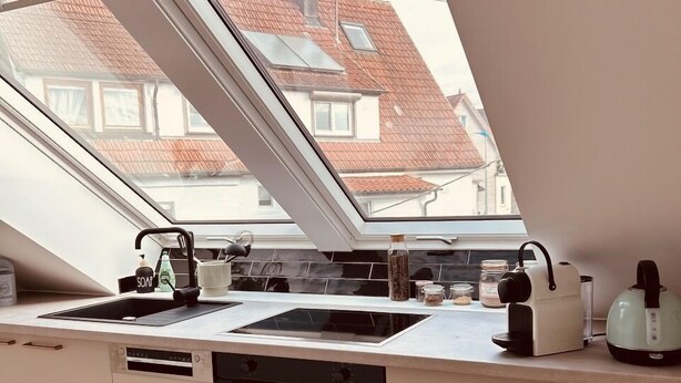 A modern kitchen with a skylight, a sink, a stove, and a countertop with various appliances.