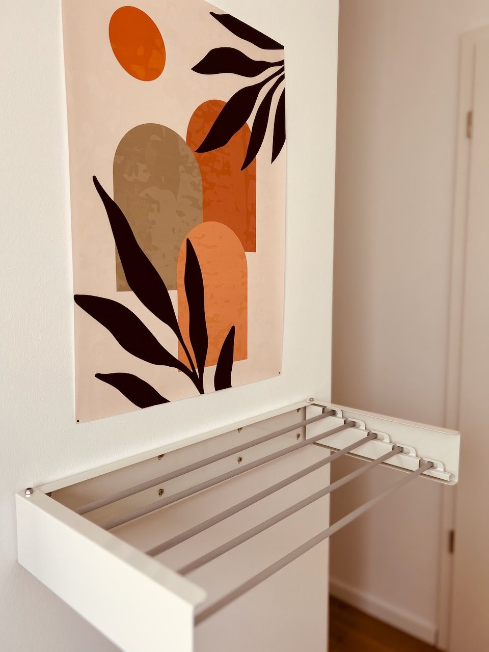 A wall-mounted drying rack with a geometric abstract painting above it.
