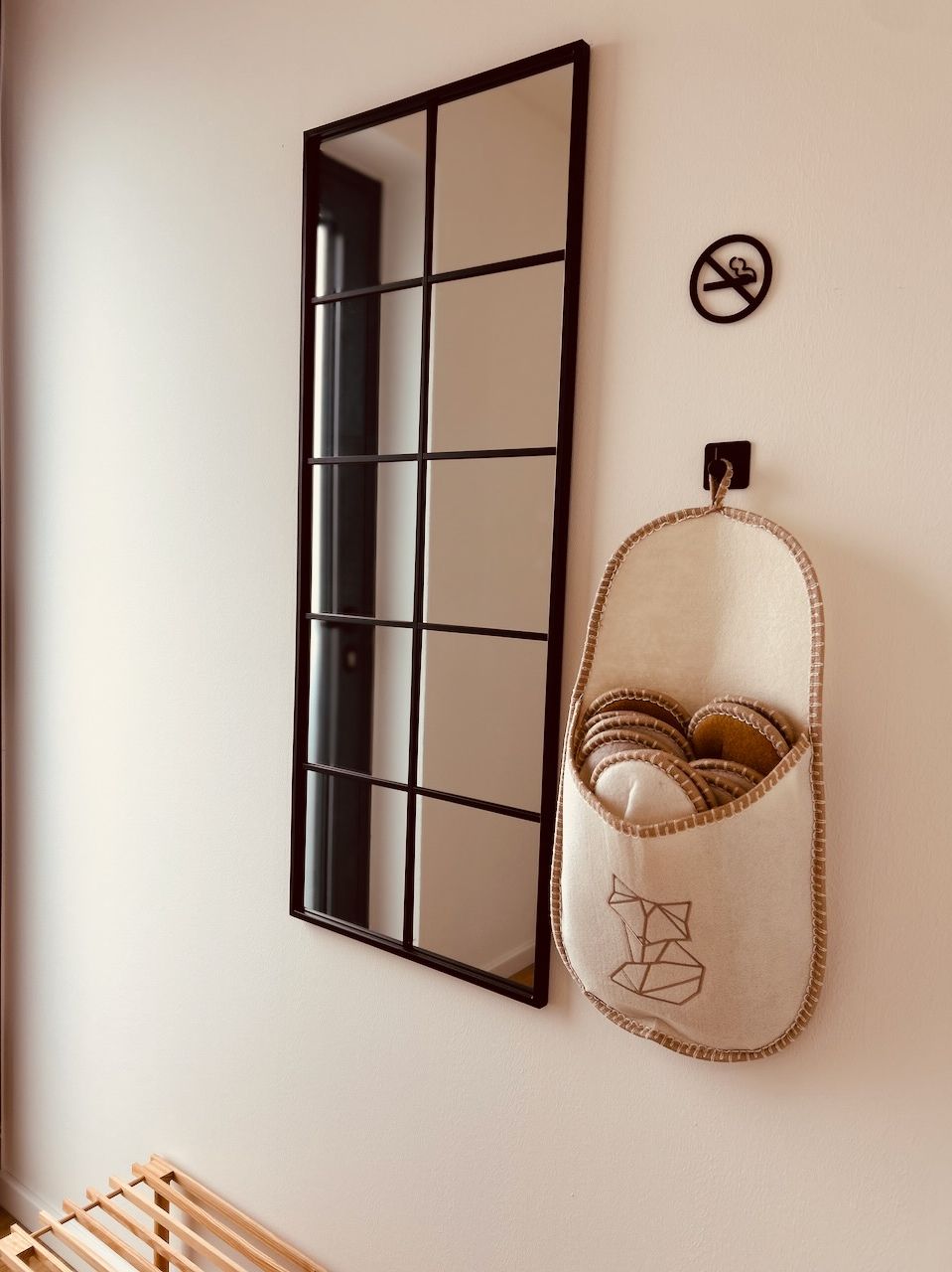 Un miroir mural orné d’un motif quadrillé, un petit panneau circulaire portant un symbole d’interdiction et un panier de rangement en tissu au motif géométrique.