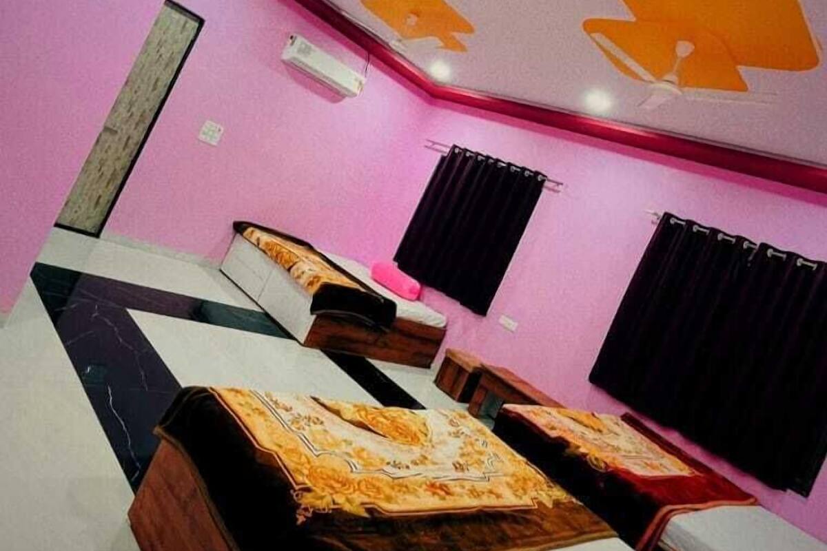 A room with a ceiling fan, two beds with wooden frames, a pink wall, and a ceiling with a geometric pattern.