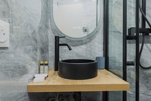 Ein modernes Badezimmer mit einem runden, schwarzen Waschbecken auf einer Holzauskładung, einem Spiegel und einer Glasdusche.