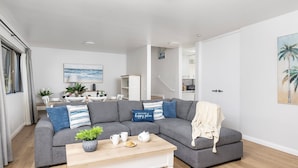 A modern living room with a grey sectional sofa, a wooden coffee table, and a kitchen in the background. - Bangalee 2 at Sunrise - waterfront apartment (Soldiers Point)