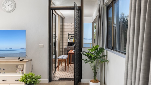 A modern living room with a large flat-screen TV, a wooden coffee table, and a comfortable seating area with a sofa and armchair. - Bangalee 2 at Sunrise - waterfront apartment (Soldiers Point)