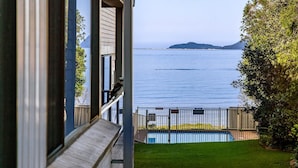 A view from a balcony overlooking a body of water with a distant island, a swimming pool, and a wooden deck. - Bangalee 2 at Sunrise - waterfront apartment (Soldiers Point)