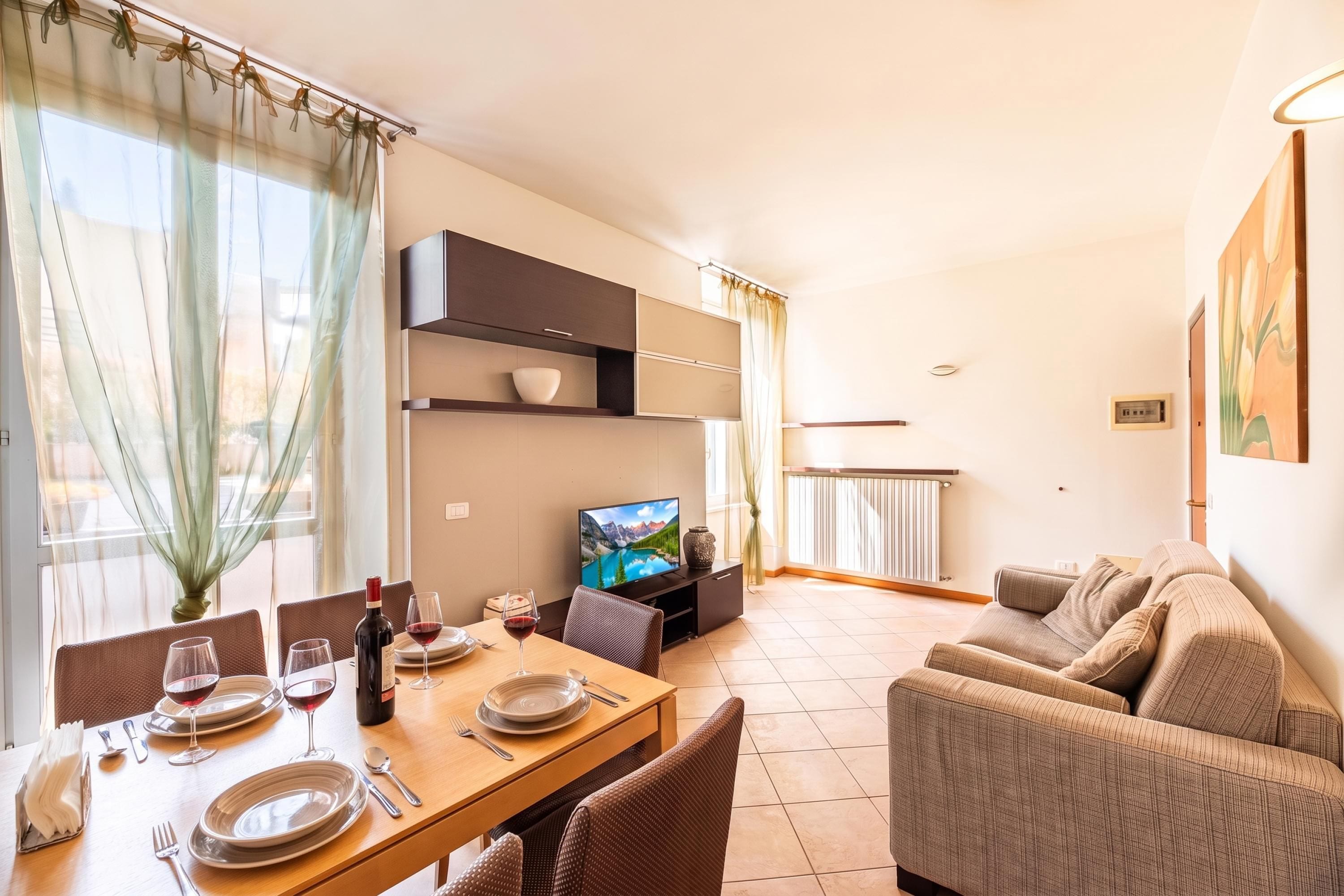 A dining area with a table set for two, a television, and a sofa.