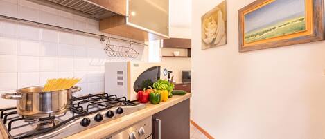Cocina moderna con estufa a gas, horno y microondas. Hay verduras frescas en la encimera, y se observa un cuadro en la pared.