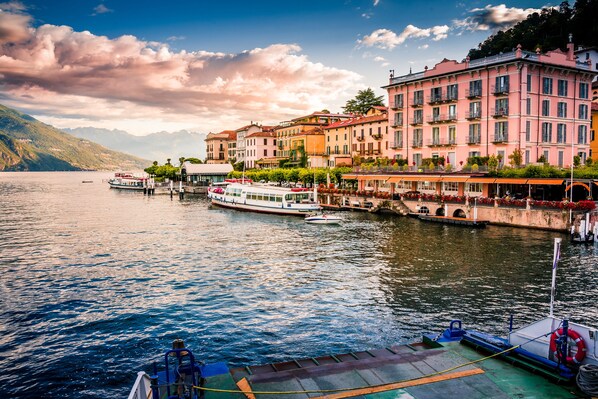 A lakeside town with buildings along the water, a boat docked at the pier, and a bridge connecting the buildings.