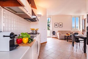 A modern kitchen with a built-in espresso machine, a dining area with a table set for two, and a living room with a sofa and a view of the outdoors. - Varenna Lake View 2 (Varenna)