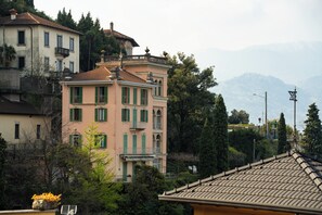 A multi-story building with balconies, surrounded by trees and mountains in the background.