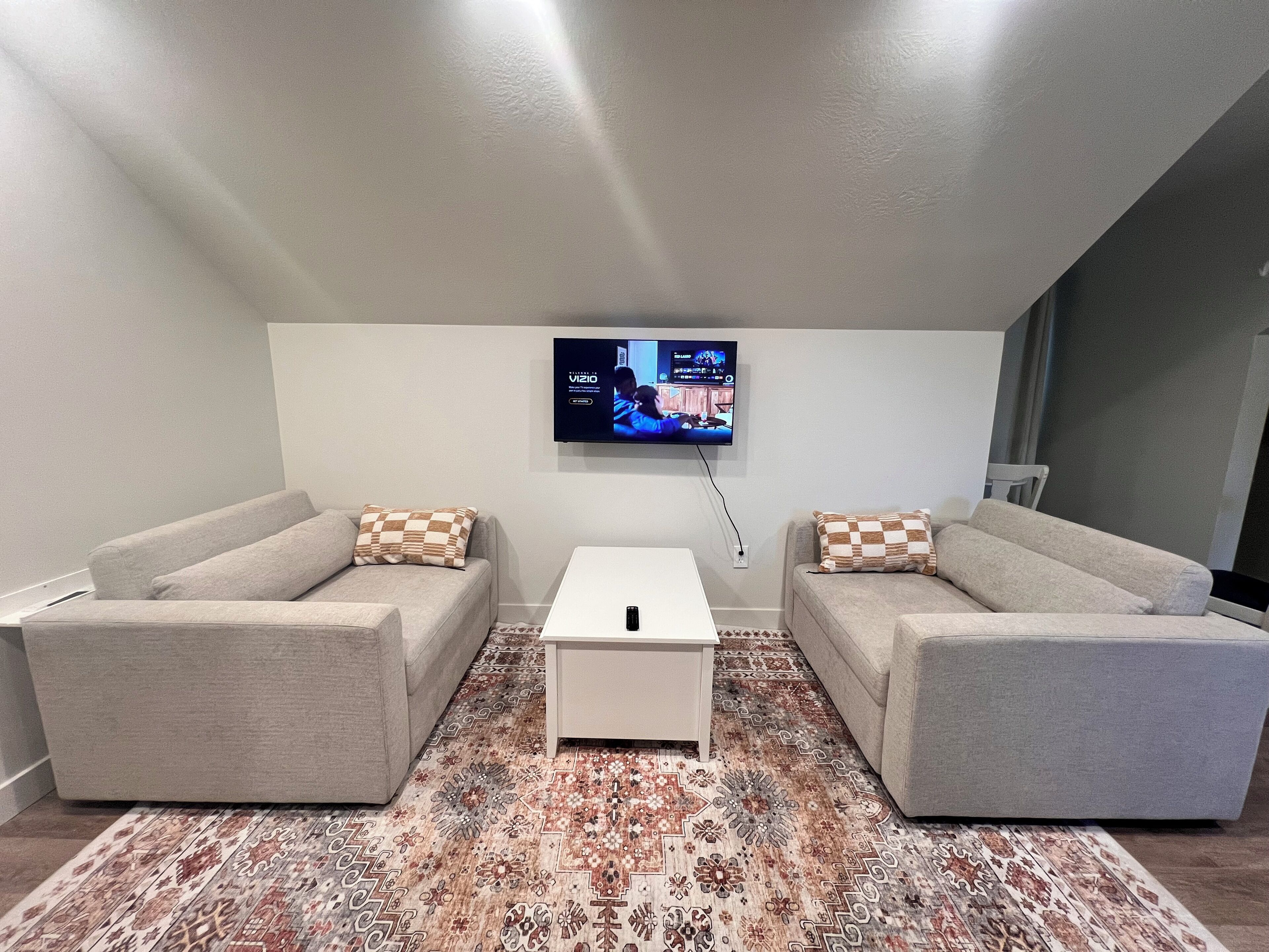 Un salon moderne avec deux canapés, une table basse et un téléviseur fixé au mur.