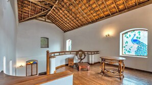 A room with a wooden ceiling, a peacock stained glass window, a wooden bench, and a small table. - Peacock House Saligao (Saligao)
