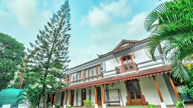 A traditional two-story building with a balcony, surrounded by lush greenery and a clear sky. - Peacock House Saligao (Saligao)