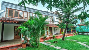 A traditional house with a tiled roof, a porch with a swing, and a well-maintained garden with potted plants and a lawn. - Peacock House Saligao (Saligao)