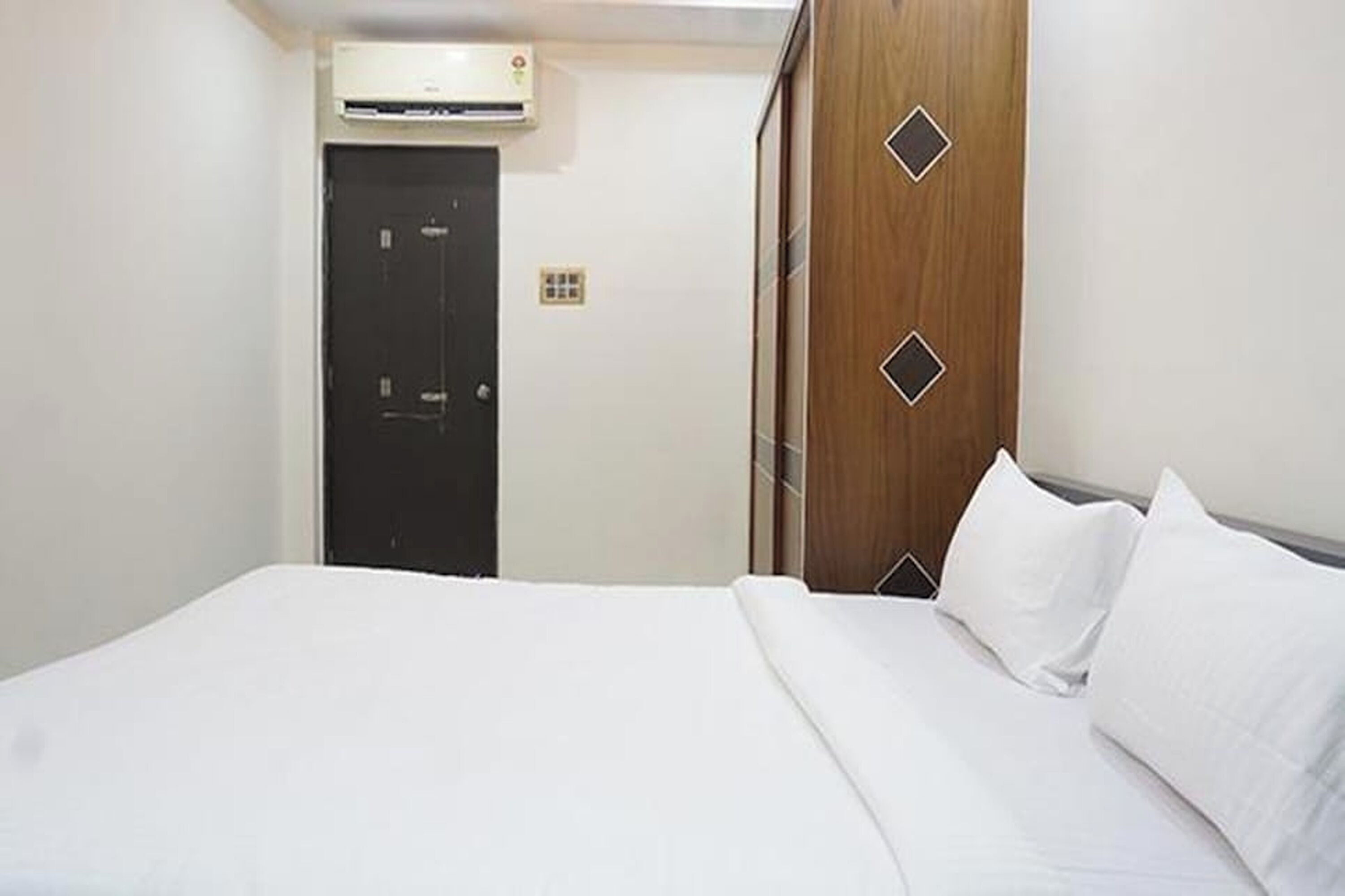 A hotel room with a bed, a wardrobe, and an air conditioning unit.
