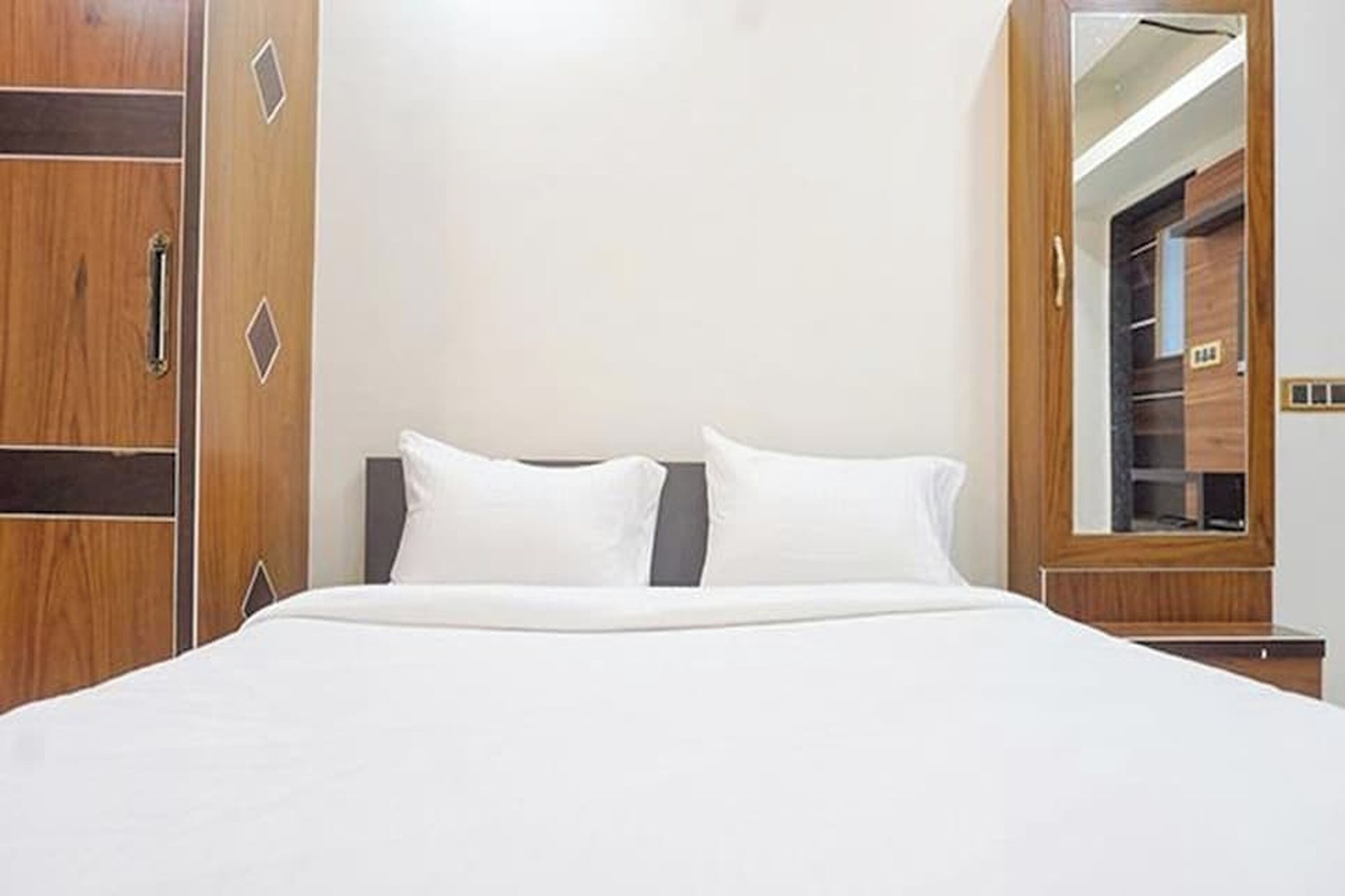 A hotel room with a large bed, wooden wardrobe, and a mirror reflecting a wardrobe.