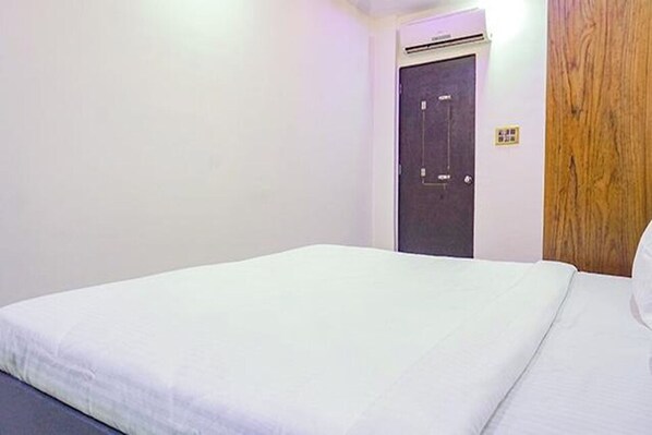 A simple room with a bed, a door, and a wooden panel on the wall. - Hotel Classic Square (Pune)
