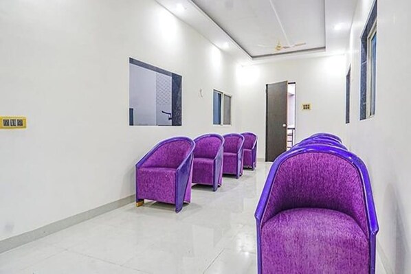 A hallway with purple chairs lined up, a white wall with a window, and a door at the end. - Hotel Classic Square (Pune)