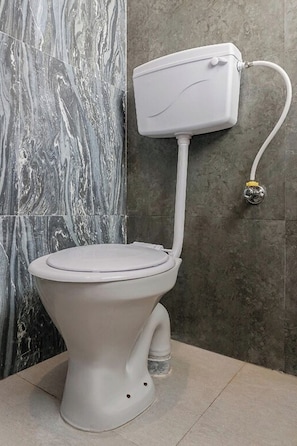 A toilet with a white tank and lid, positioned against a wall with grey and white marble tiles. - I Suites (Pune)