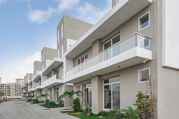 A modern residential building with multiple balconies, large windows, and a paved walkway. - I Suites (Pune)