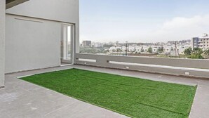 Un balcón con una zona de césped artificial verde, suelo de hormigón y vistas a un paisaje urbano con edificios al fondo.