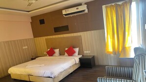 Una habitación de hotel con cama, sillón, equipo de aire acondicionado y ventana con cortinas.
