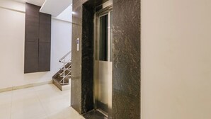 Egy modern lift márványfalakkal, fém korláttal és csempézett padlóval.