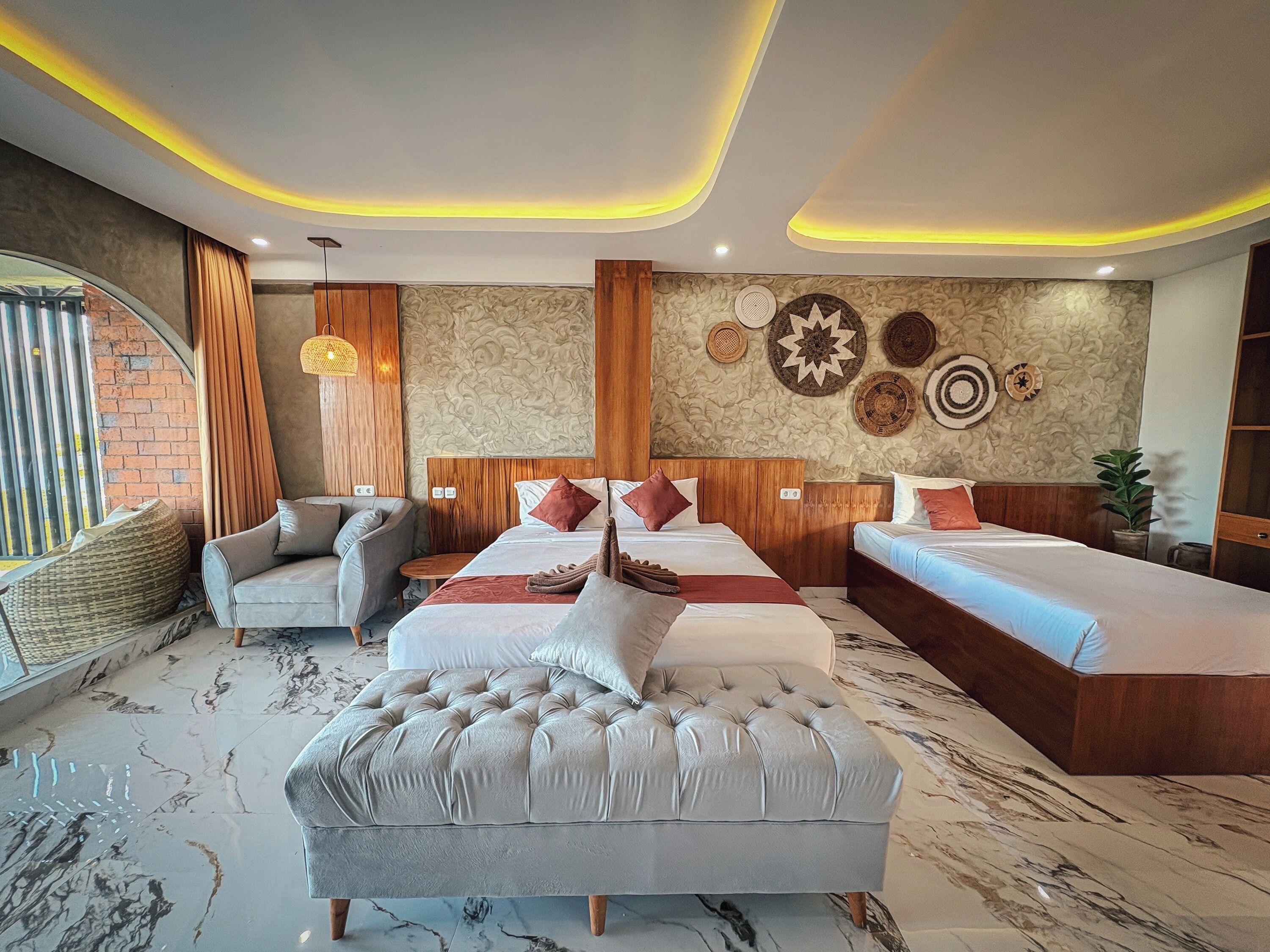 A modern hotel room with a marble floor, two beds with headboards, a grey sofa, and decorative wall art.