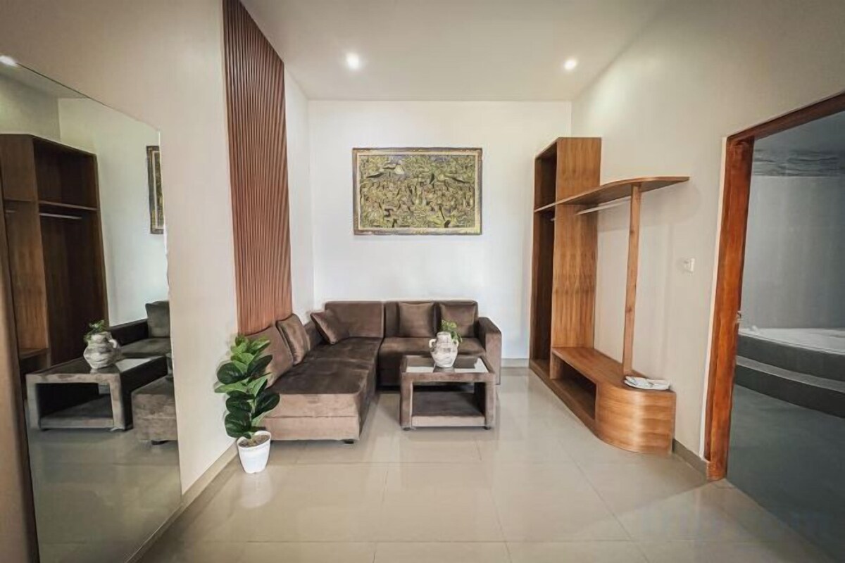 A living room with a sectional sofa, two side tables, a potted plant, a wooden shelf, and a large mirror.