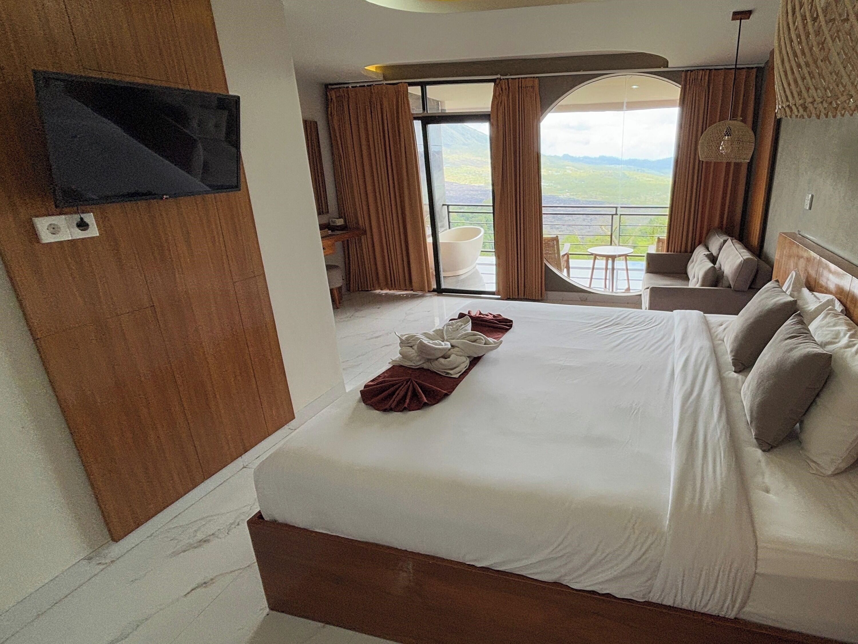 Una habitación de hotel con una cama grande, un televisor montado en la pared y un balcón con vistas al paisaje.