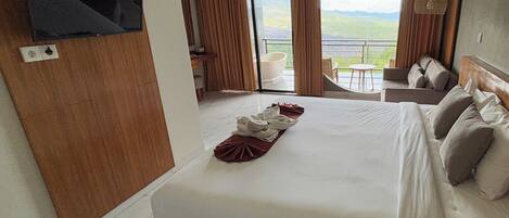 Una habitación de hotel con una cama grande, un televisor montado en la pared y un balcón con vistas al paisaje.