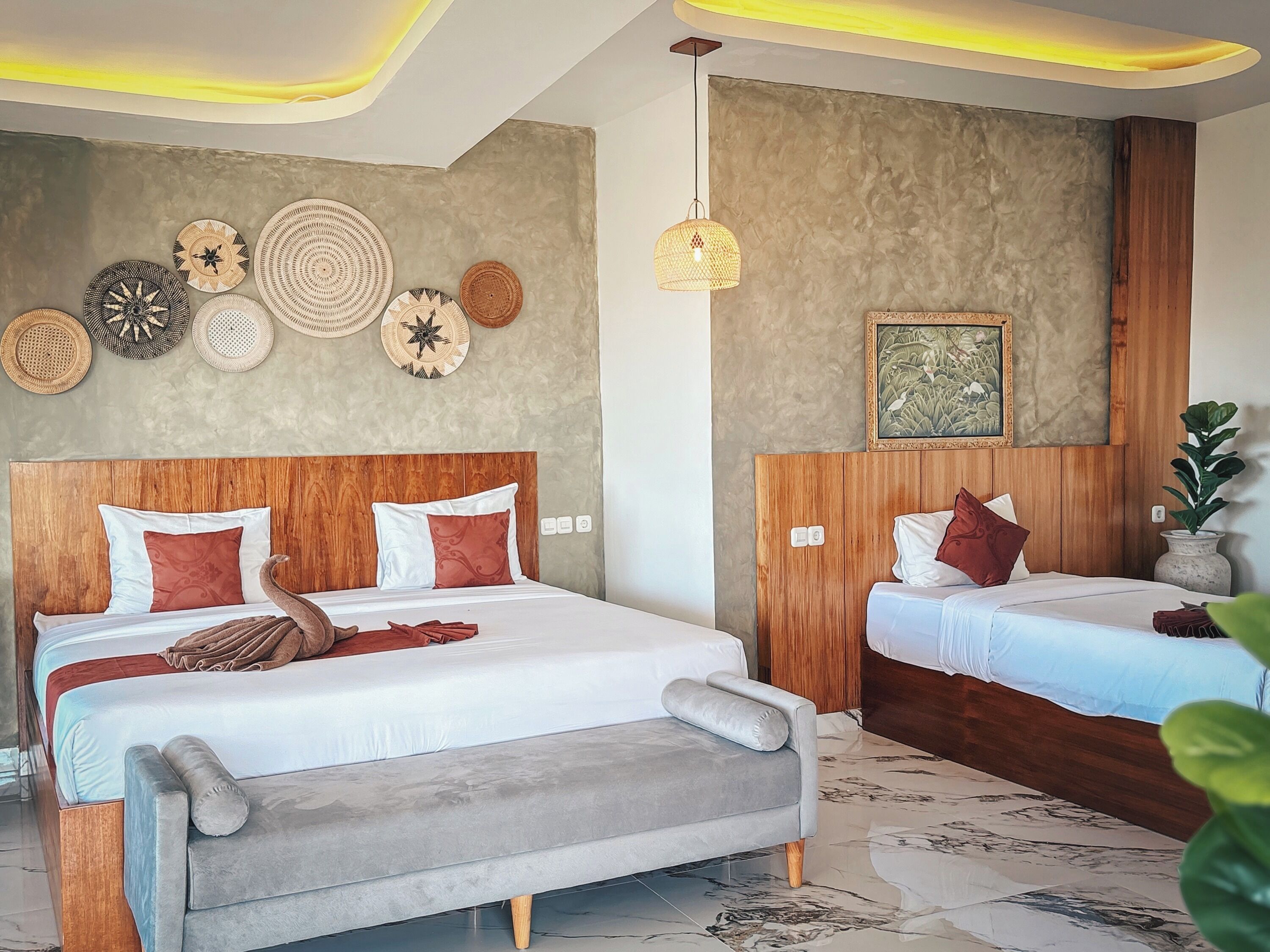 Une chambre d’hôtel avec deux lits, un canapé gris, un mur décoré de paniers tressés, un luminaire suspendu et un tableau encadré.