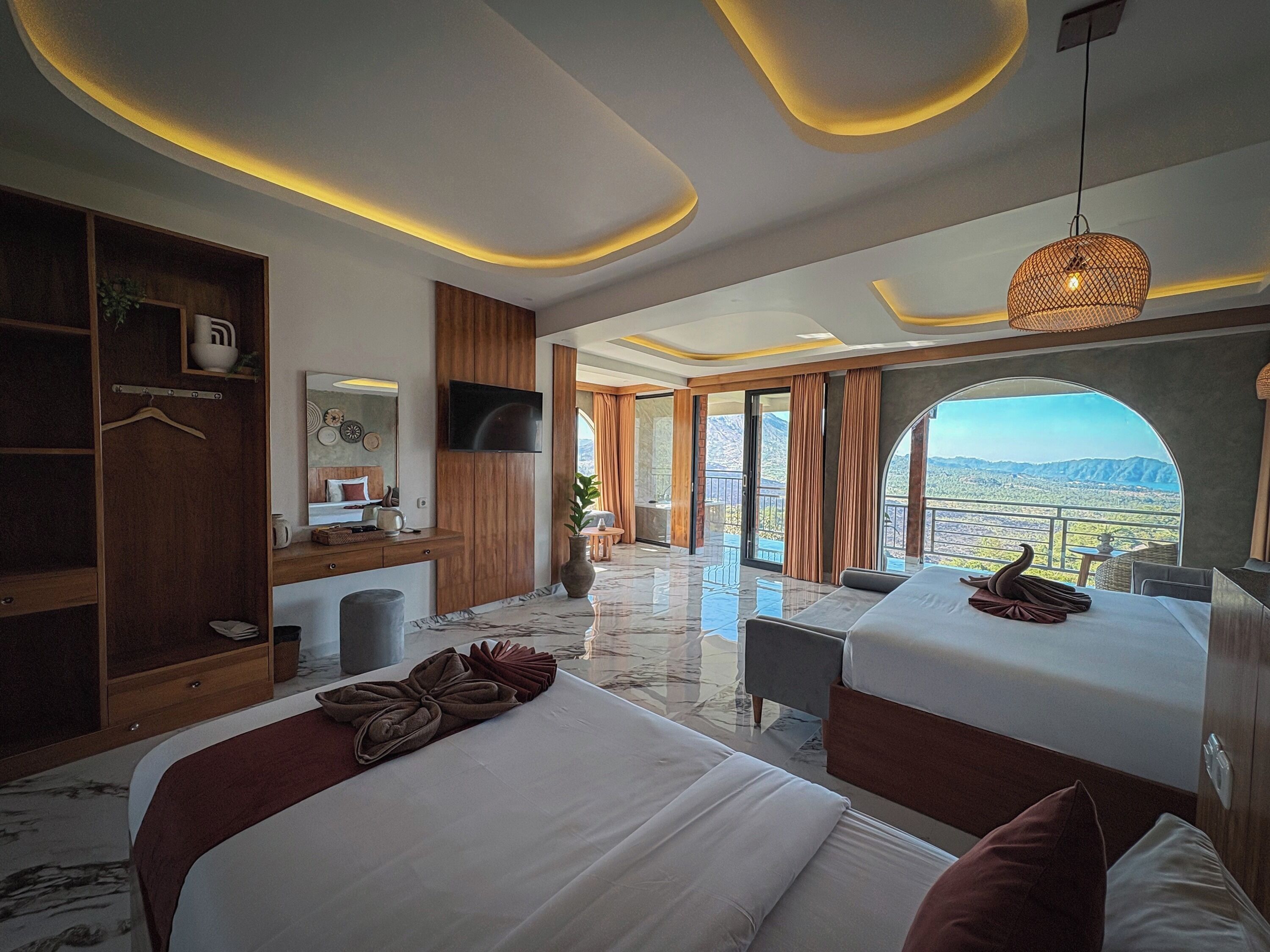 A modern hotel room with two beds, a TV, a desk, and a large window with a mountain view.