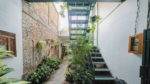 A narrow alleyway with a brick wall, potted plants, and a metal staircase. - Omah Gerjen 29 (Yogyakarta)