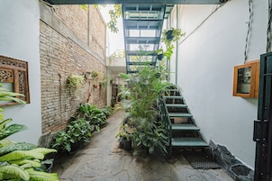 Un estrecho callejón con un muro de ladrillo, plantas en macetas y una escalera de metal.