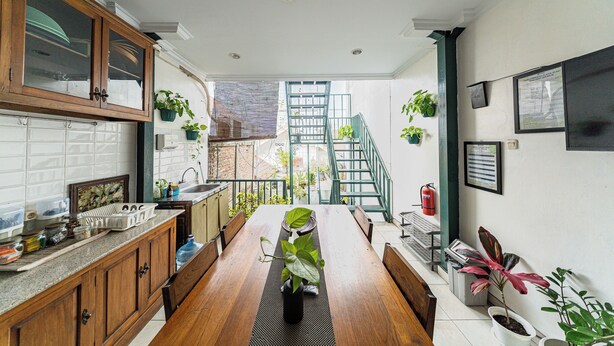 A kitchen with wooden cabinets, a dining table with a plant centerpiece, and a staircase leading to an upper level. - Omah Gerjen 29 (Yogyakarta)