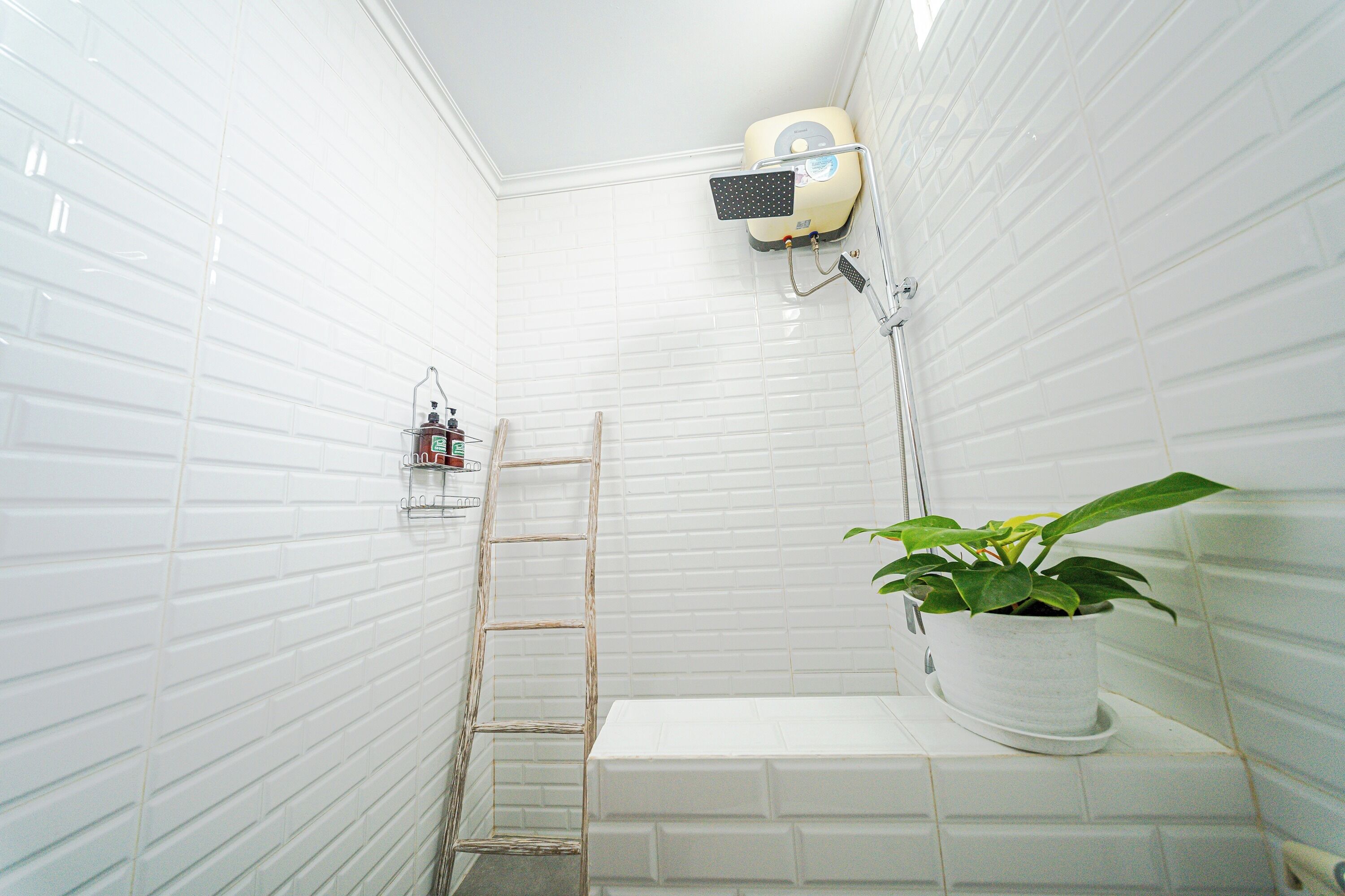 A bathroom with white tiled walls, a shower, a ladder, a potted plant, and a shelf with toiletries.