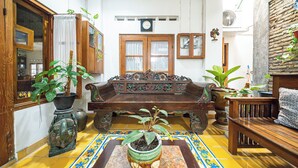 A traditional room with a wooden sofa, a small table with a potted plant, and a tiled floor with a decorative border. - Omah Gerjen 29 (Yogyakarta)