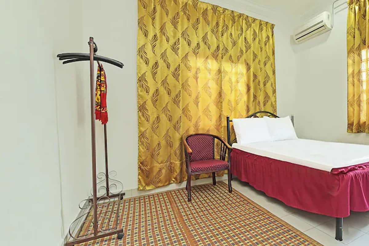 A hotel room with a bed, a chair, a drying rack, and patterned curtains.