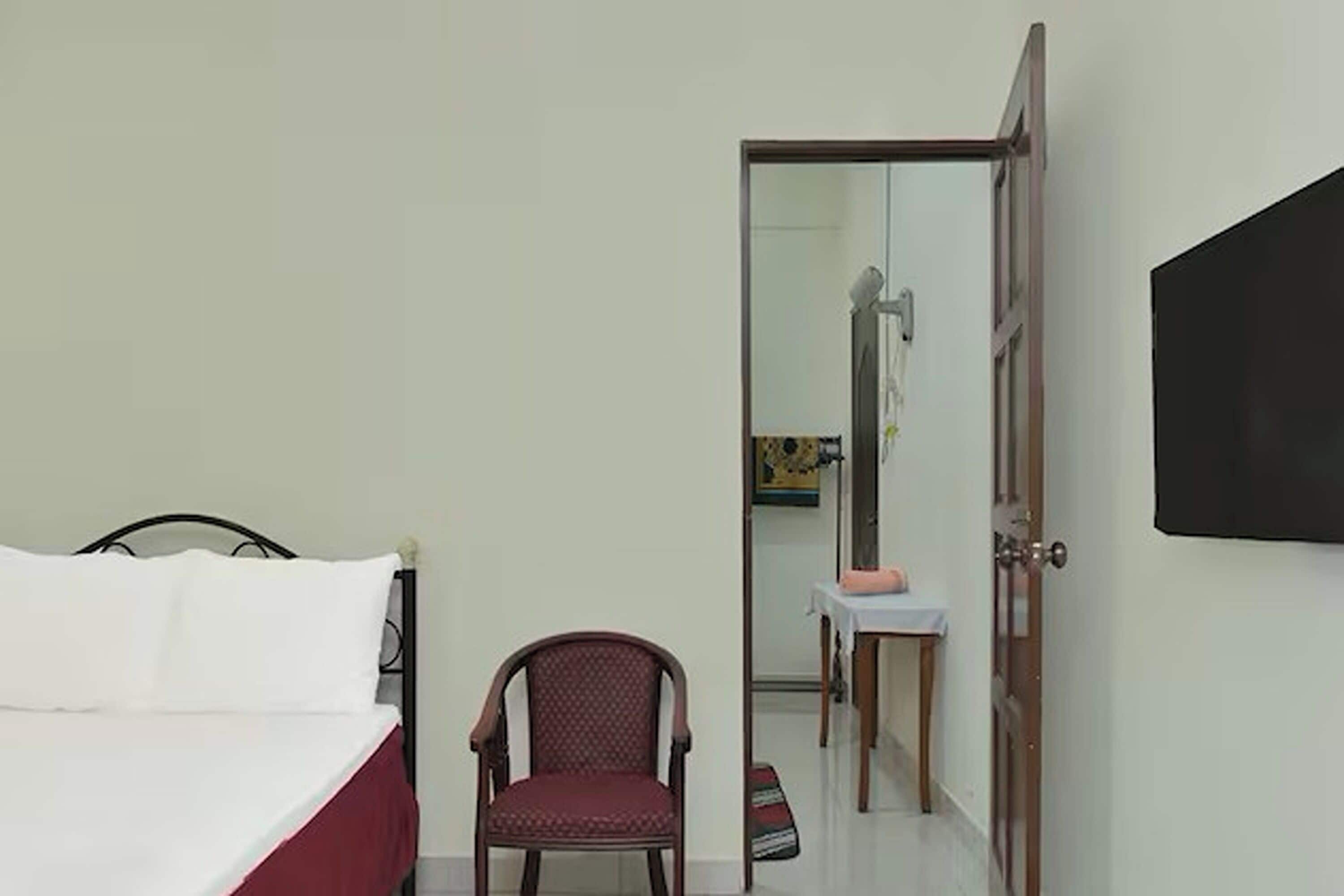 Un dormitorio con cama, una silla, una mesita y una puerta que da a un baño.