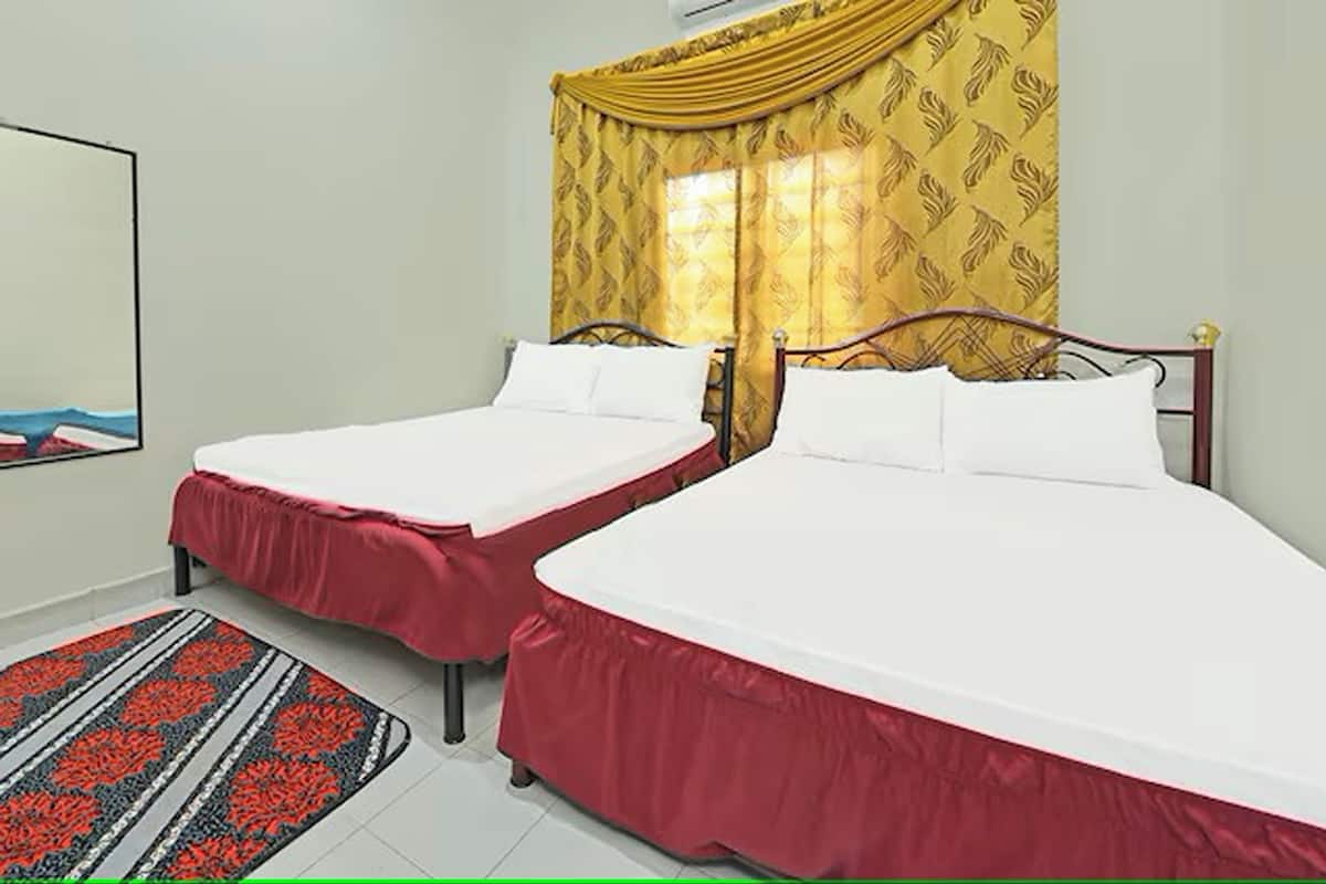 A hotel room with two single beds, a large window with yellow curtains, and a red and black patterned rug.