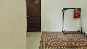 Una habitación con puerta cerrada, un tapete estampado y un soporte metálico con tela.